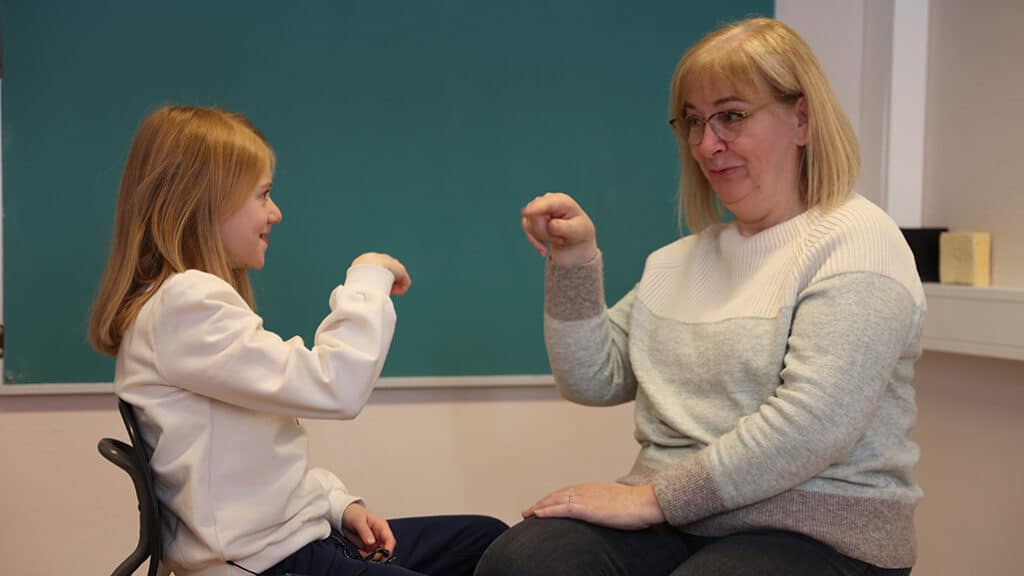 Emma  med sin tegnspårklærerer hjemme i Harstad. De sitter overfor hverandre og bruker tegnspråk